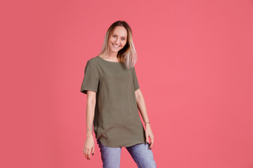 Playful young woman is spinning while shooting in a studio in a khaki oversized t-shirt on a pink background. Advertising space