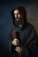 Medieval monk in robe holds spellbook in hands