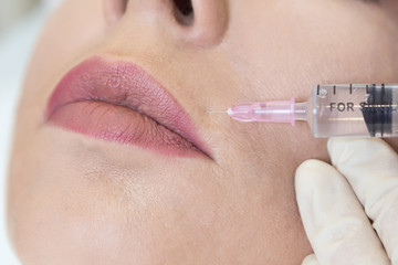 Closeup of adult woman gets filler injection in her lips in beauty clinic