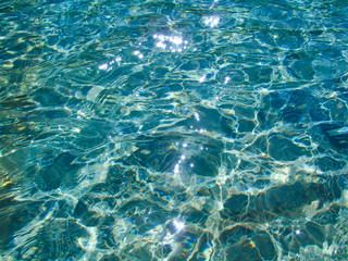 Fototapeta na wymiar Blue transparent water surface with bright sun glare and sunny shining reflections on bottom. Top view of turquoise ripple texture with sunlight refracting through liquid layer.