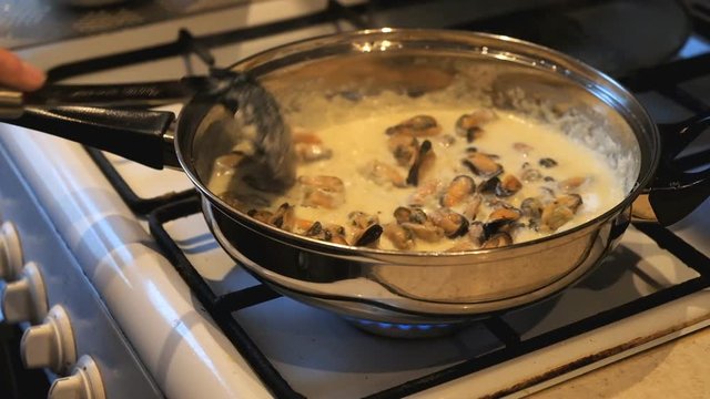 Woman cooks mussels in a cream sauce in a frying pan.