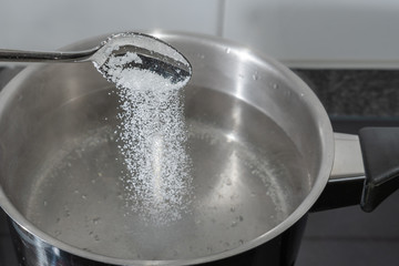 Salz in das Kochende Wasser im Topf schütten