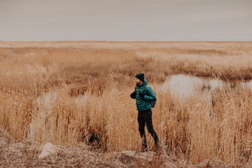 Sideways photo of attractive male dressed in fashionable hat, jacket and trousers, carries rucksack, stands outdoors, has unforgettable journey, enjoys autumn time. People, rest and lifestyle concept