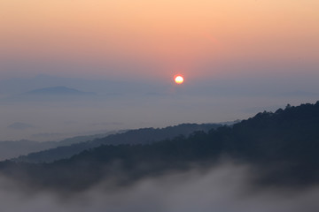 Mountain valley in misty day with red sun