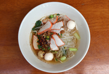 Rice stick noodles soup with red roasted pork in the bowl on the wooden table.