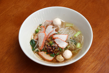 Rice stick noodles soup with red roasted pork in the bowl on the wooden table.