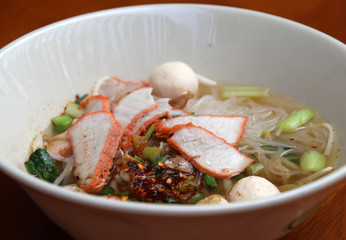 Rice stick noodles soup with red roasted pork in the bowl on the wooden table.
