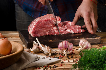 Butcher cutting pork on wooden board on a wooden table on the dark background