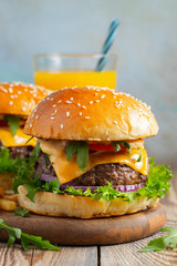 Two fresh homemade burgers with fried potatoes and orange juice on a wooden table