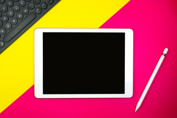 Tablet pencil and keyboard on background two tone with yellow and pink copy space for text