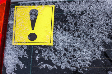 The yellow exclamation mark on the back window of the car covered by snow