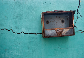 Teal textured wall, with long traversing crack and a rusted metal mailbox
