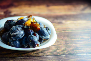 Frozen organic plums without stones on a white plate and a rustic wooden table.  Healthy food concept.