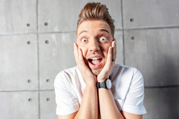 A young attractive funny joyful emotional man winks in a white shirt and a butterfly, on a gray background