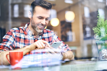 Man sitting in cafe during winter time and looking at smartphone