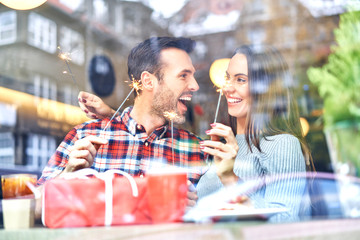 Couple playing with sparklers while sitting with present in cafe during Christmas time