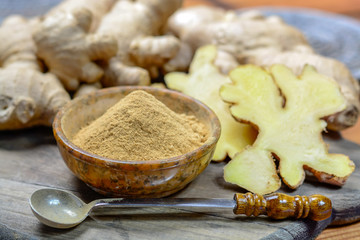 Fresh raw ginger root and bowl with ginger powder close up