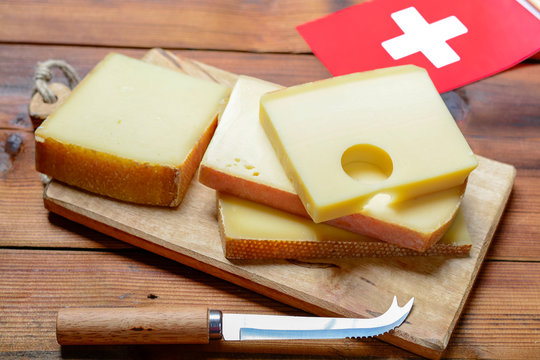 Assortment Of Swiss Cheeses Emmental Or Emmentaler Medium-hard Cheese With Round Holes, Gruyere, Appenzeller And Raclette Used For Traditional Cheese Fondue And Gratin And Flag Of Switzerland