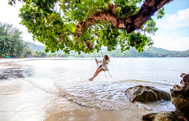 Beautiful young woman traveler swinging on a swing on a tropical island in the background of...
