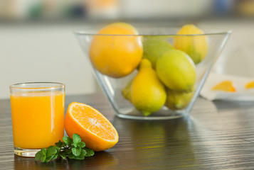 Glass of freshly squeezed orange juice with bowl of fruits on the background.