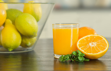 Glass of freshly squeezed orange juice with bowl of fruits on the background.