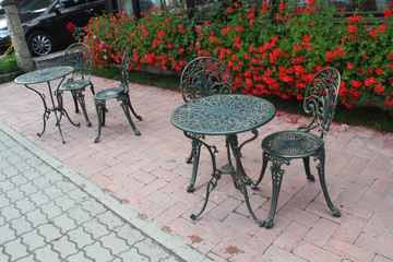 Fototapeta na wymiar Forged table and chairs with ornament on the background of flowers in a cafe in the city of Bran, Romania
