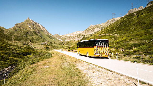 Public transportation in the mountains of switzerland named Postauto. Yellow bus on the road.