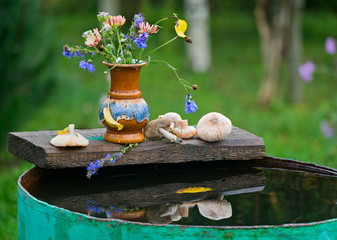 Autumn still life in the country bouquet of flowers and wild mushrooms on a barrel of water.