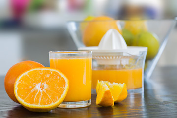 Glass and juicer with freshly squeezed orange juice with bowl of fruits on the background.