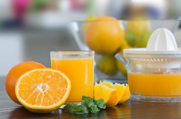 Glass and juicer with freshly squeezed orange juice with bowl of fruits on the background.