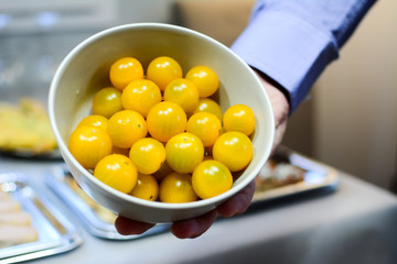 The male hand in a white bowl shows organic yellow cherry tomatoes. The concept of healthy organic food and nutrition.