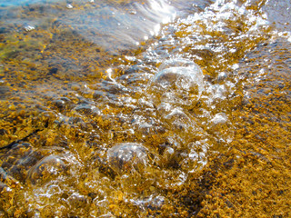 Transparent water and pebbles beach - close-up. Summer background image of sunlight reflecting and glistening on the water surface and wet small stones in foreground.