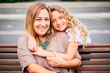 mommy and daughter hugging with love and happiness together on a bench in outdoor leisure activity - family with caucasian woman and girl people cheerful