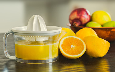 Glass and juicer with freshly squeezed orange juice with bowl of fruits on the background.