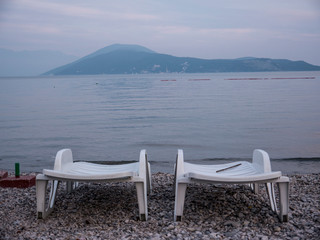 Two empty plastic chaise lounge on sea side at the end of season side view