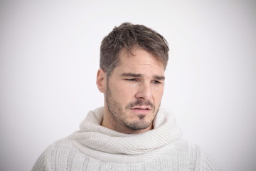 Obraz premium Sad facial expression of a man in a white sweater in front of a white background