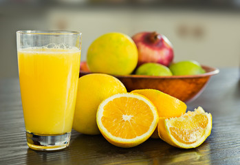Glass of freshly squeezed orange juice with bowl of fruits on the background.