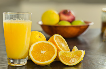 Glass of freshly squeezed orange juice with bowl of fruits on the background.