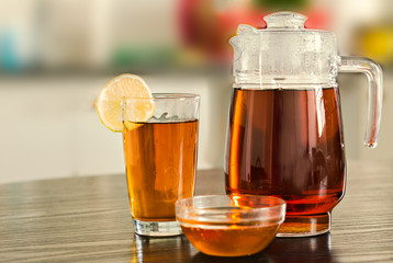 Pitcher with glass of hot black tea with bowl of honey and fruits  and lemons on kitchen background.
