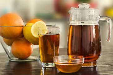 Pitcher with glass of hot black tea with bowl of honey and fruits  and lemons on kitchen background.