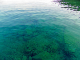 Transparent water surface through which is seen a texture of the bottom. Top view of the calm sea, lake, river, pond. Natural blue - green beautiful background image.