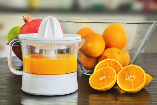 Juicer with freshly squeezed  orange juice and whole and sliced oranges.