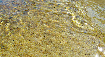 Transparent water surface with golden sun glare and sunny shining reflections on the sand. Top view of yellow ripple texture with sunlight refracting through liquid layer.