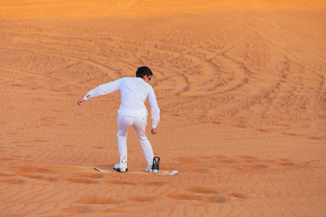 Tourist having fun sandboarding on desert dunes in Dubai safari