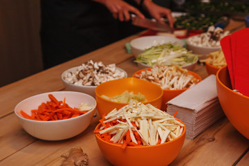 Sliced salad ingredients in various bright deep plates on a light wooden table