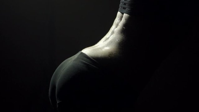 A young girl in black underwear slowly pours water on her back in the dark on a black background. Close-up of wet back of sexy girl in lingerie. Sexy ass.