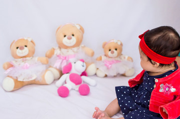 Fototapeta na wymiar Baby in red and blue clothes looking at teddy bears blurred in the background