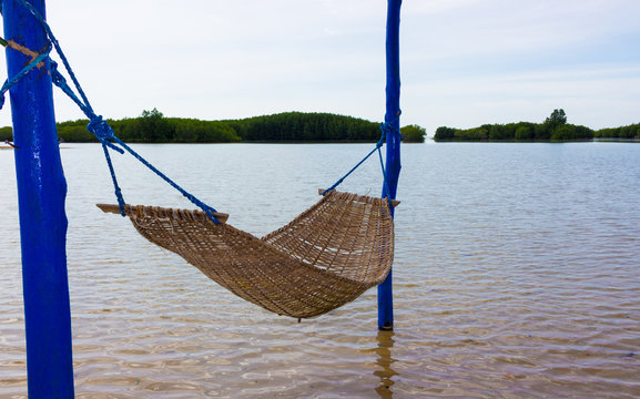 Wicker empty hammock in the shade in the shallows of a tropical island in the sea against the background of mangroves. Enjoying the summer. Perfect summer background for advertising paradise travels