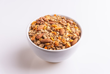Granola or muesli with nuts and rasins in a white bowl on a white background, angle view, soft light