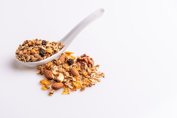 Granola or muesli with nuts and rasins in a white spoon on a white background, angle view, copy space, soft light